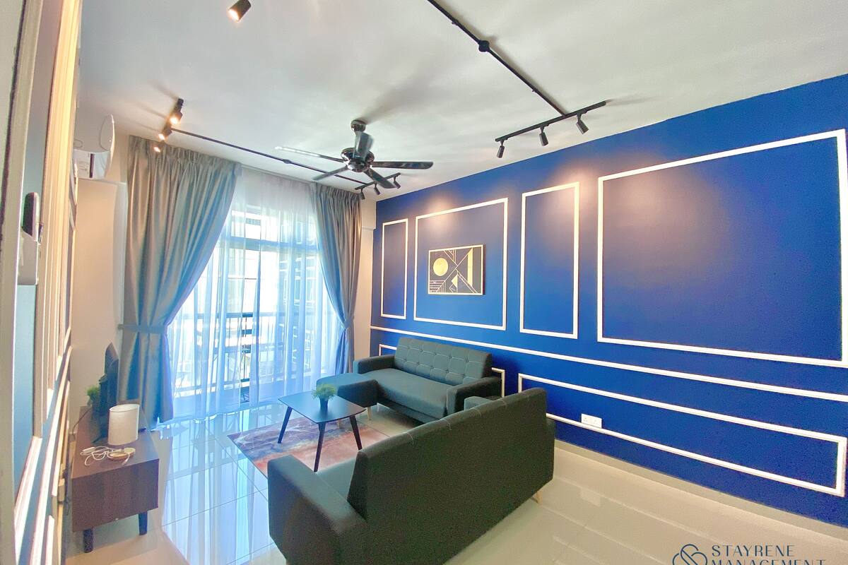 Ein modernes Hotelzimmer mit blauer Akzentwand, Deckenventilator und einer Sitzecke mit Sofa und Sesseln.