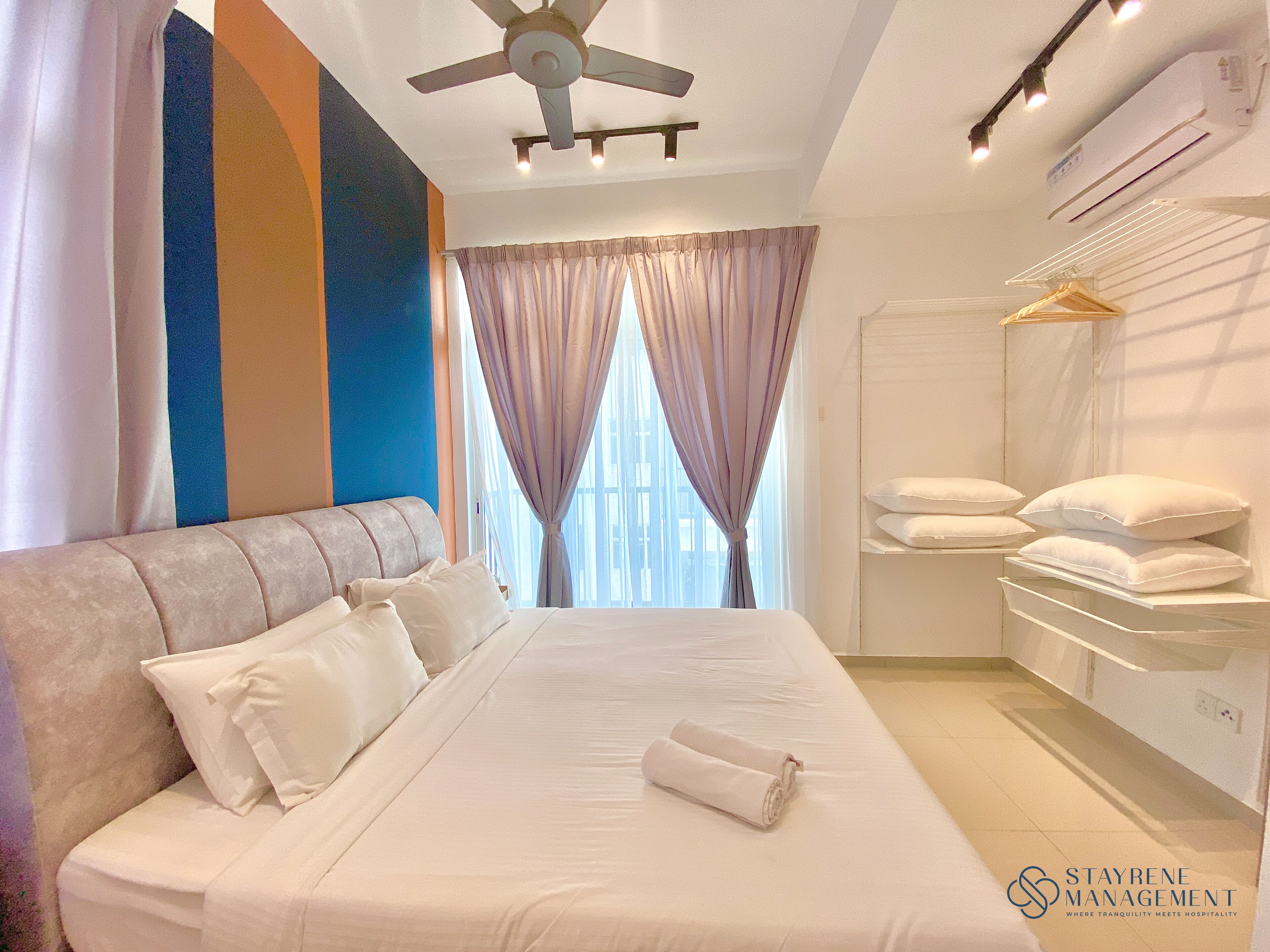 Une chambre d’hôtel avec un grand lit, un ventilateur de plafond, une fenêtre avec des rideaux et un porte-serviettes fixé au mur.