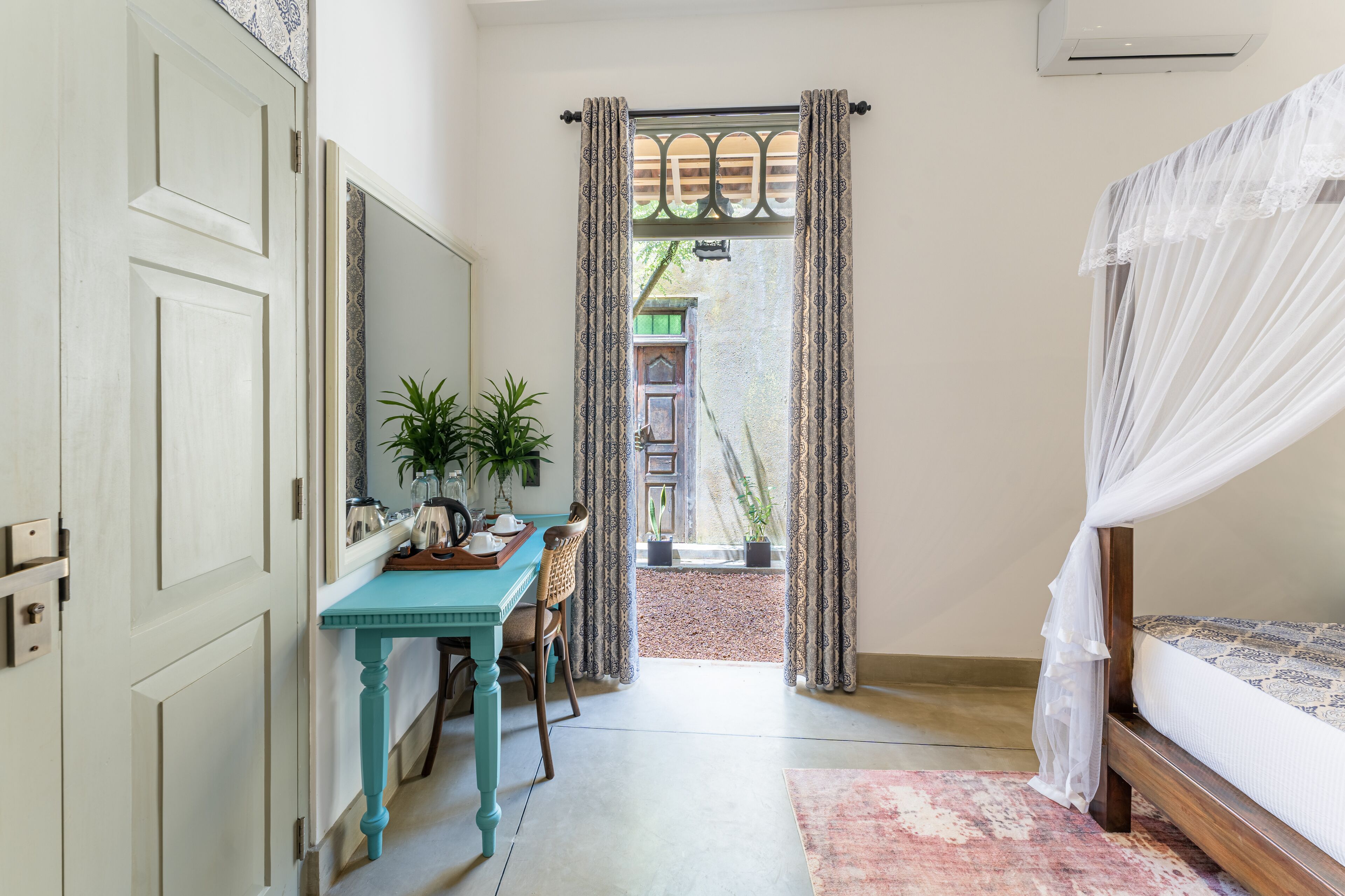 A bedroom with a bed, a desk with a chair, a window with curtains, and a view of the outside.