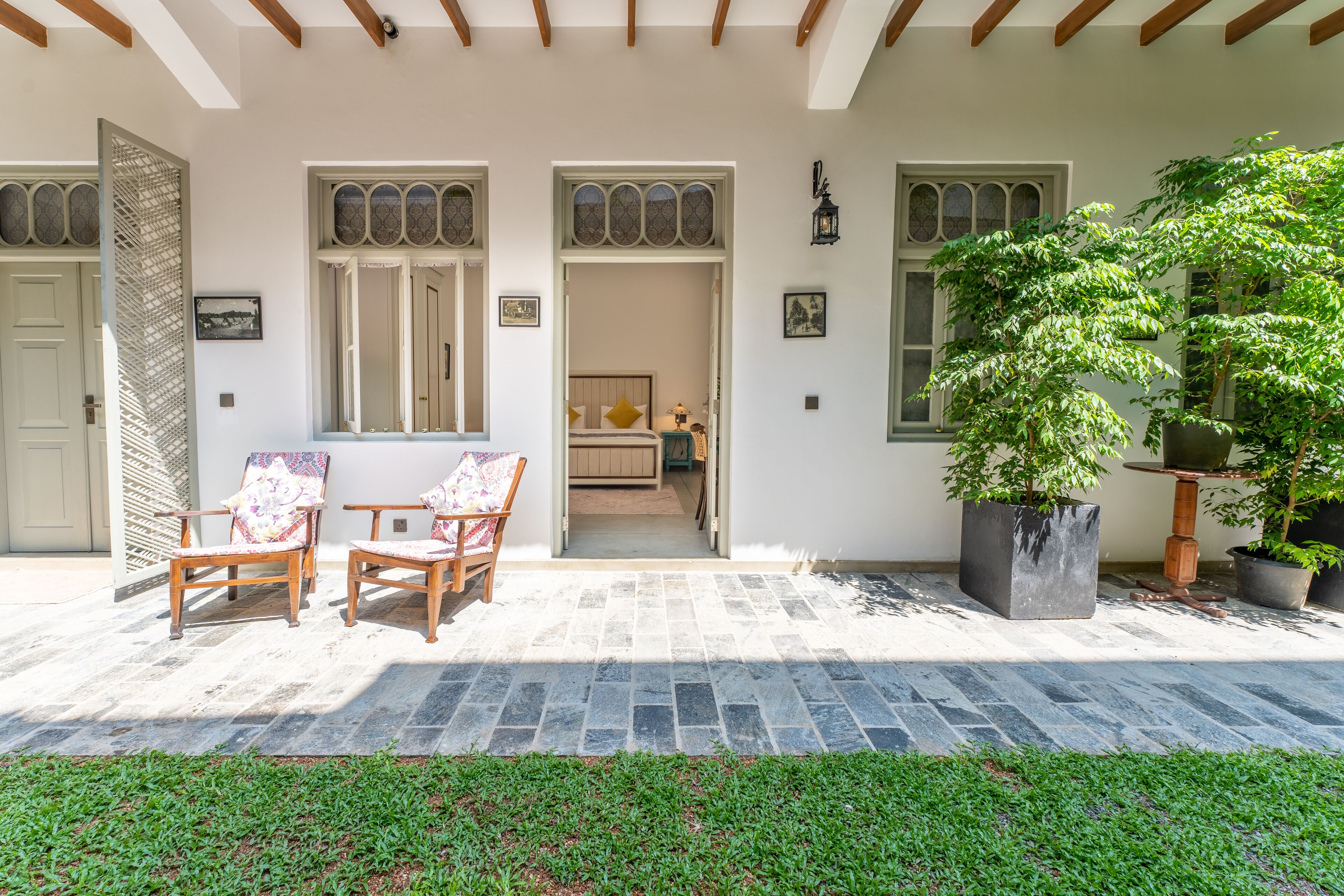 Un patio techado con dos sillas de madera, una planta en maceta y suelo de piedra.