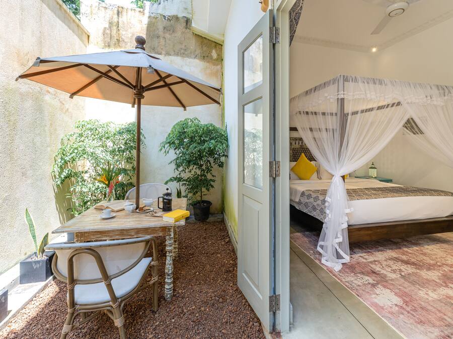 A room with a bed, a table with chairs, an umbrella, and a potted plant.