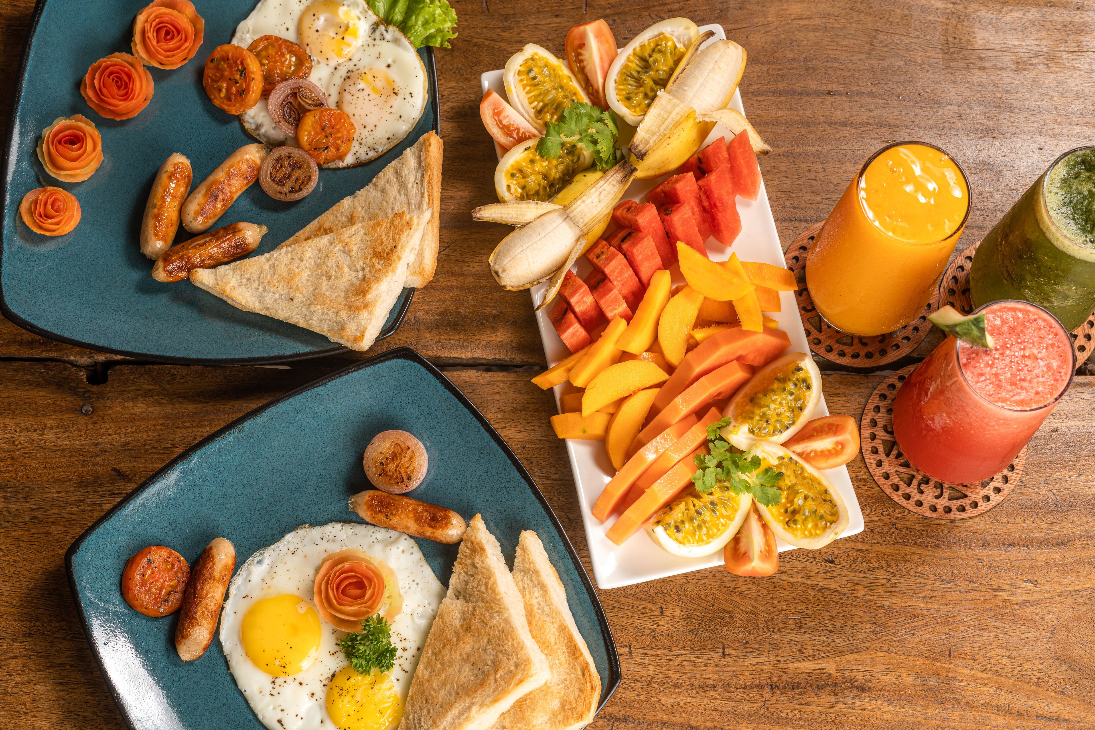 A breakfast spread with eggs, sausages, toast, and various fruits and vegetables on a wooden table.