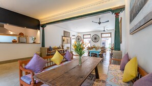 A spacious dining area with a wooden table, cushioned chairs, and a bench with colorful cushions. - The Fort House (Galle)