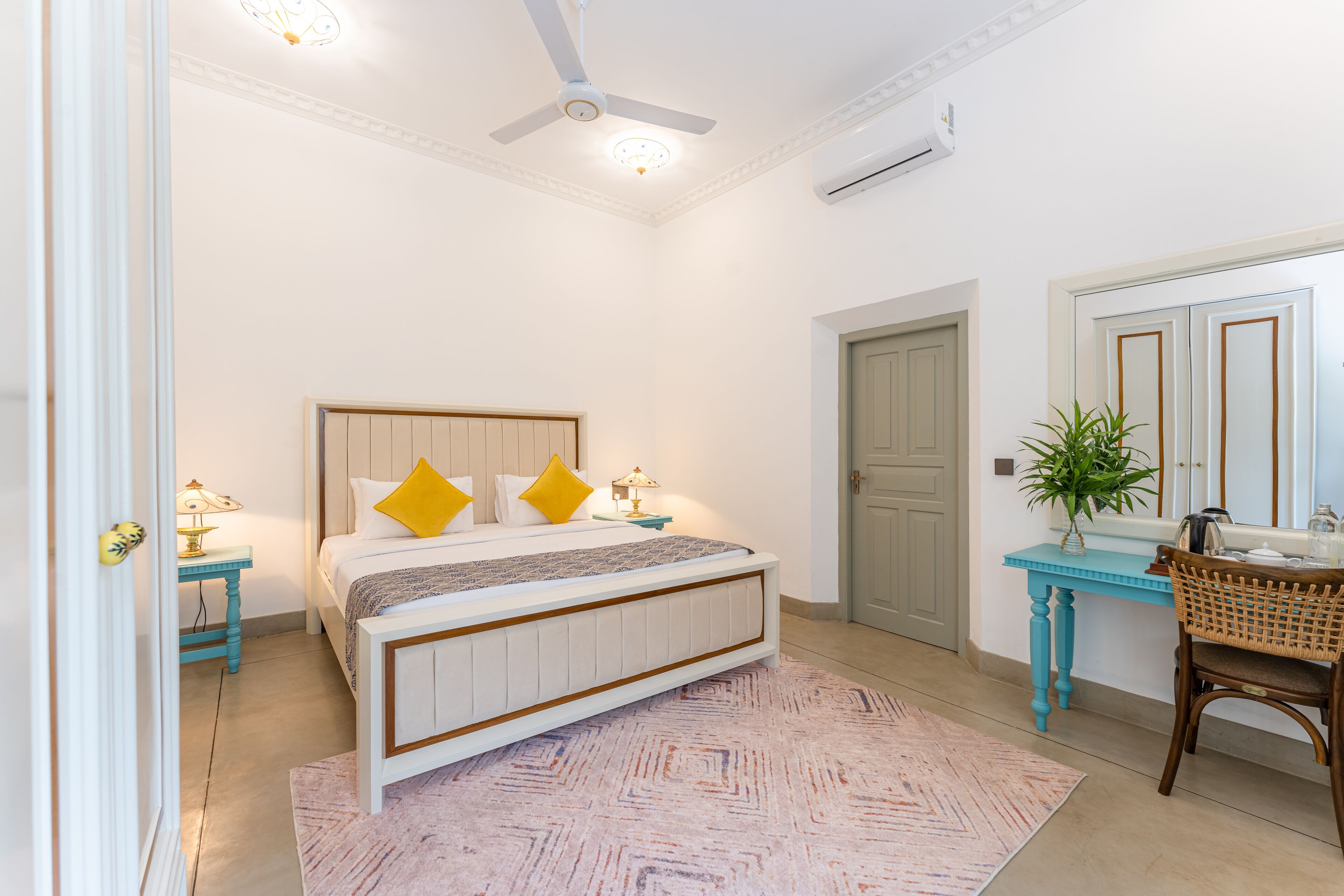 Ein Schlafzimmer mit einem Bett, Nachttischen, einem Deckenventilator, einer Klimaanlage, einem Schreibtisch mit Stuhl und einer Topfpflanze.
