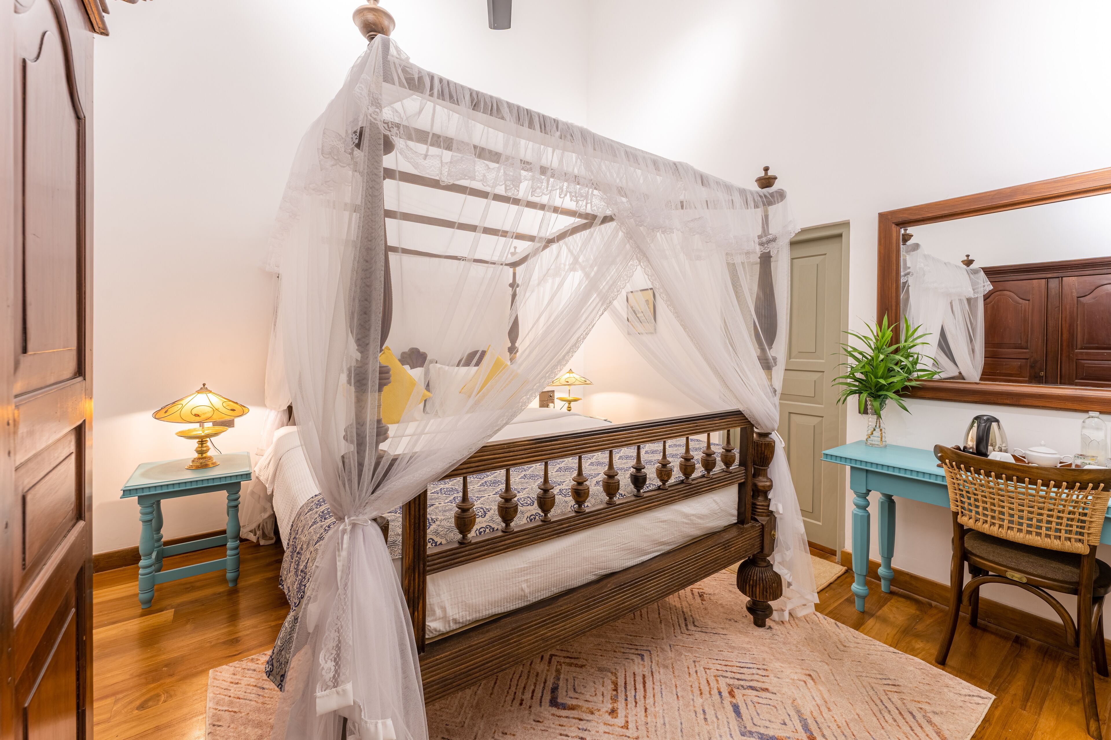 A four-poster bed with a canopy, a bedside table with a lamp, a chair, and a small table with a plant.