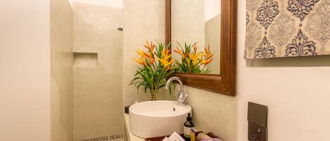 A bathroom with a white sink, a mirror, a tray with toiletries, and a shower area.