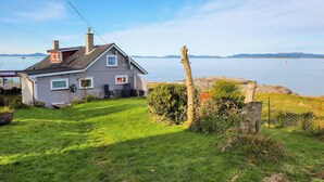 A house with a sloped roof, a chimney, and a satellite dish. There is a grassy yard with a fence and a wooden post. - Amazing home in Rennesøy with house sea view (Rennesøy)