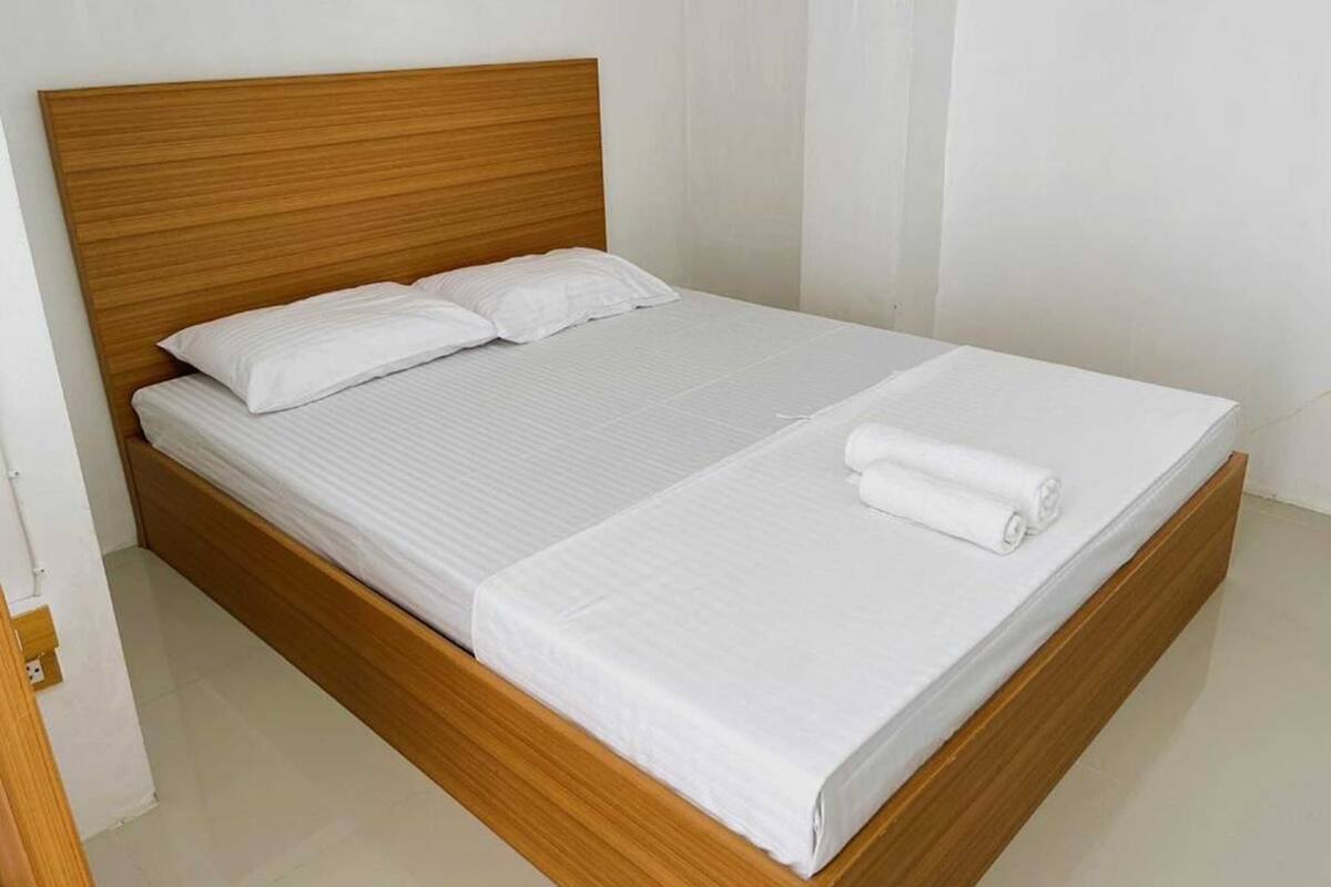 A single bed with a wooden headboard, white bedding, and a rolled towel on the footboard.