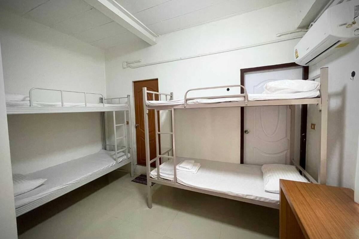 A dormitory room with bunk beds, a wooden desk, and a door.