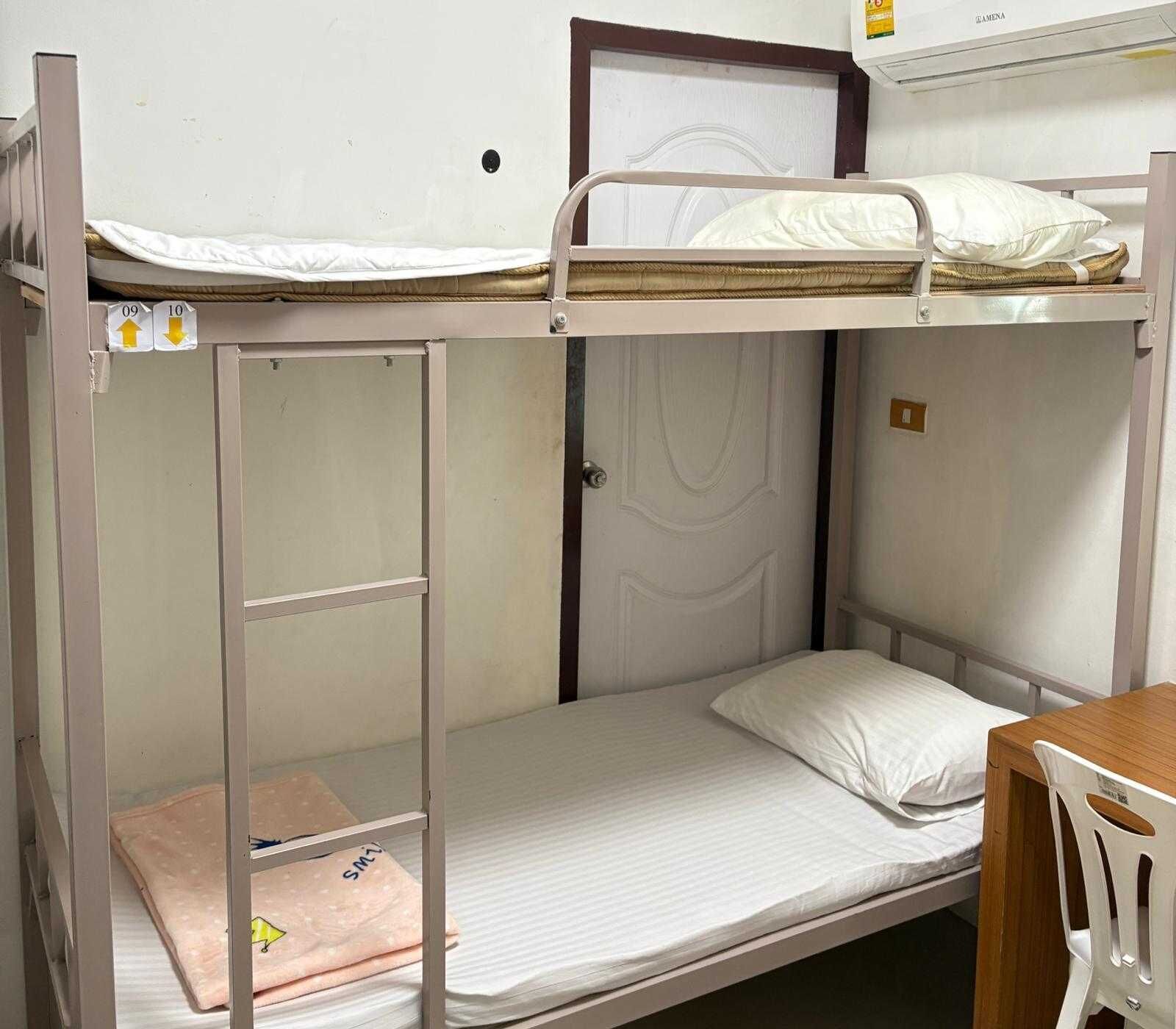 A bunk bed room with a desk and chair, a door, and a small shelf with a towel.