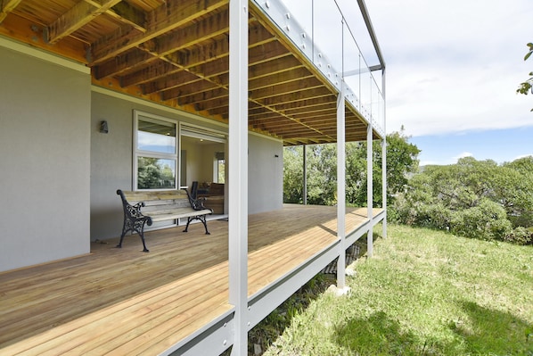 Um espaço ao ar livre coberto, com deck de madeira, bancos e vista para o verde.