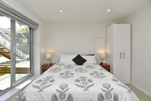 Quarto com cama grande, guarda-roupa, mesa de cabeceira e janela com vista para um deck de madeira.