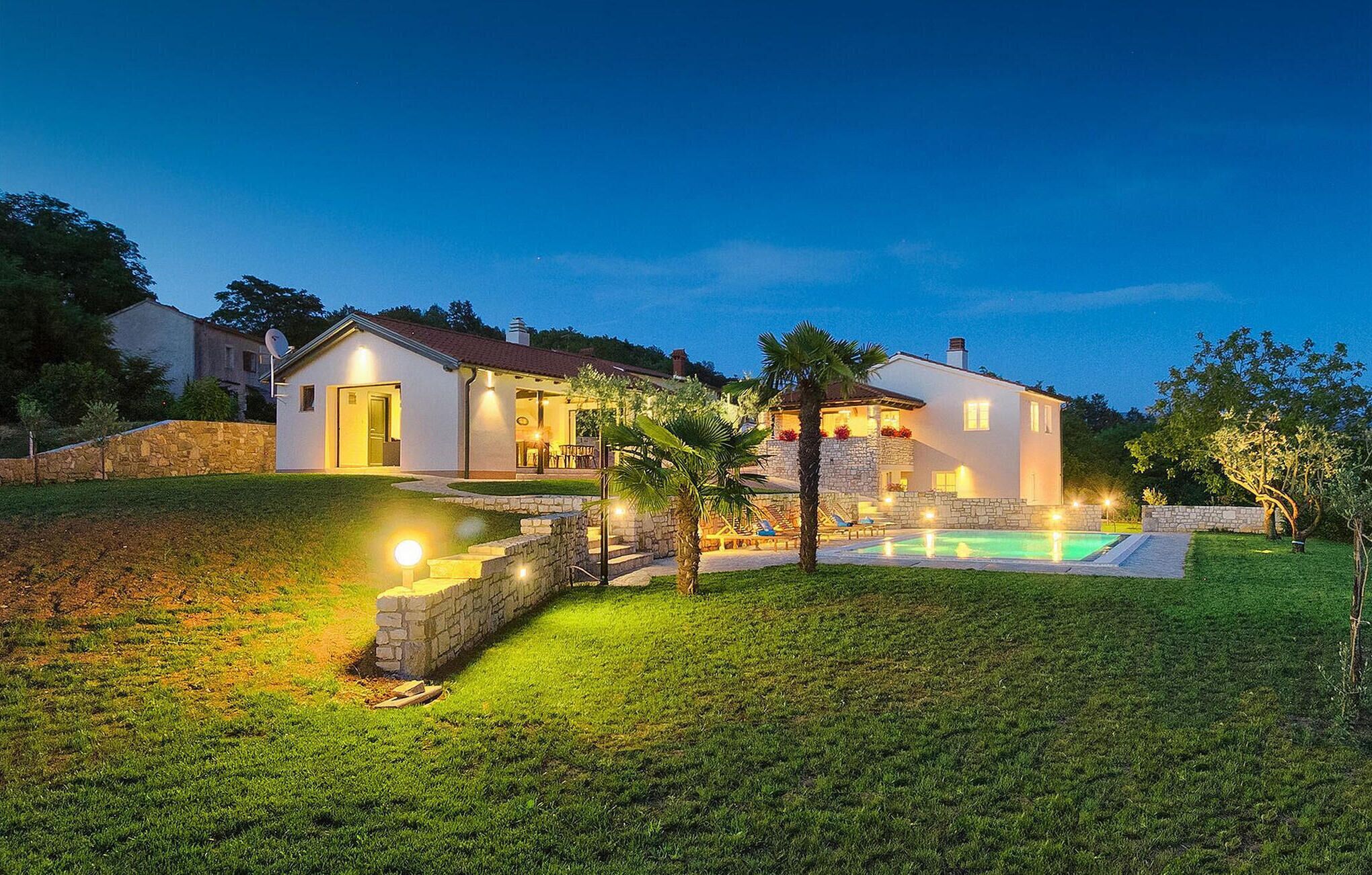 A two-story house with a swimming pool, stone walls, and a well-lit outdoor area.