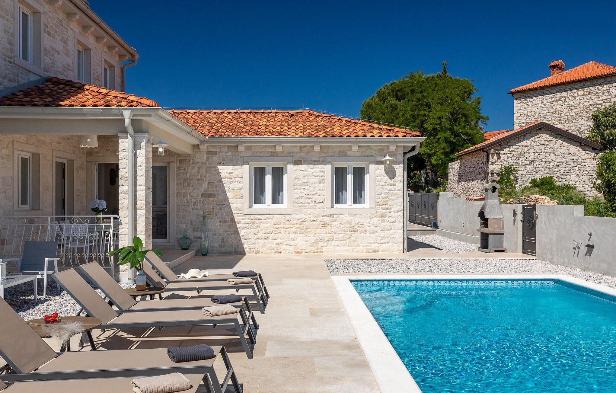 Una zona de piscina amb gandules, un edifici de pedra i una piscina blava i cristal·lina.