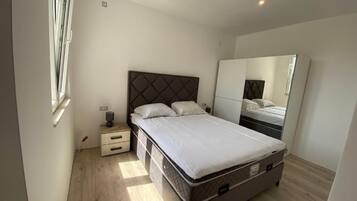 Un dormitorio con cama, mesita de noche, cómoda, espejo y armario.