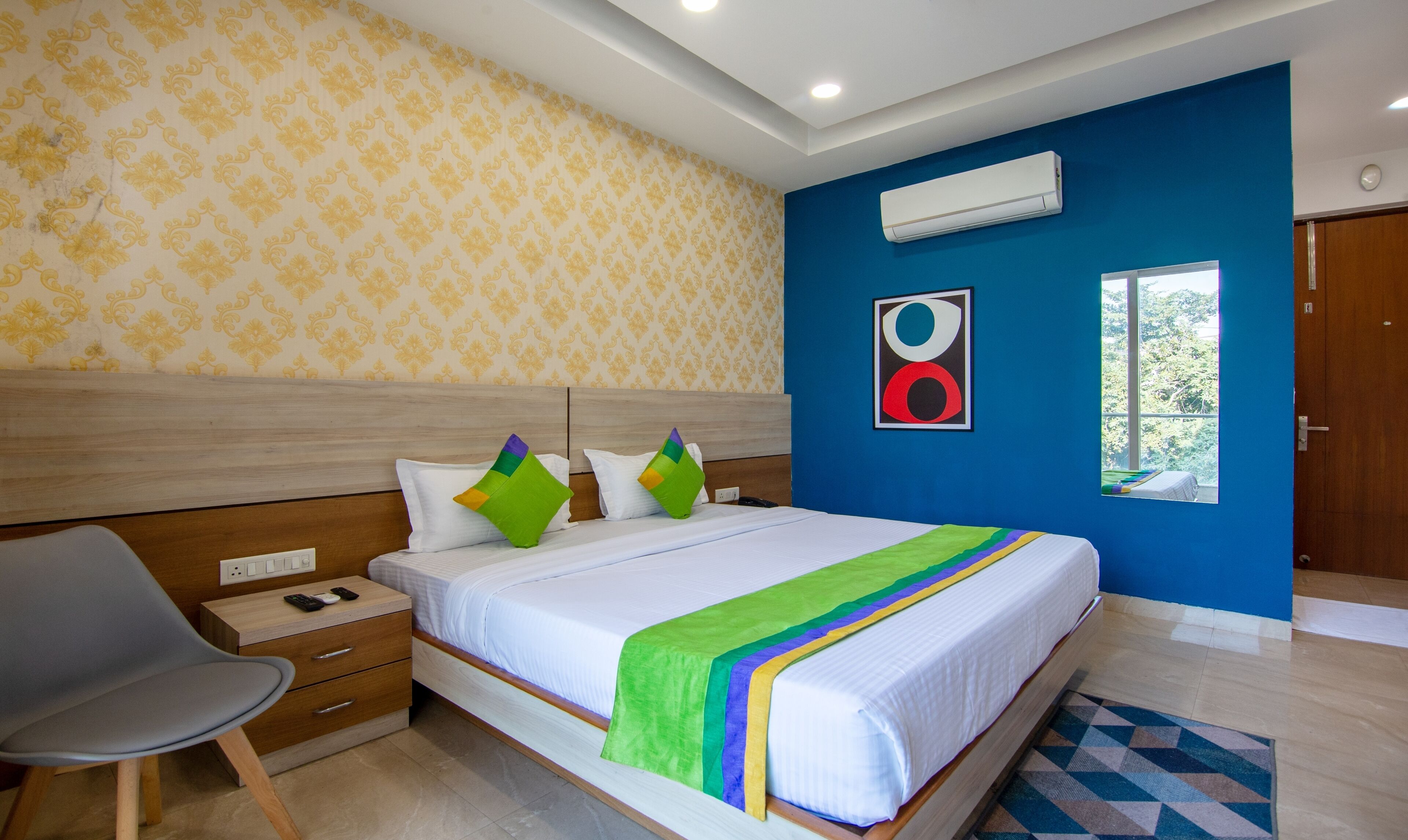 Une chambre d’hôtel équipée d’un lit, d’une chaise, d’une table de chevet, d’un climatiseur et d’une fenêtre donnant sur un paysage verdoyant.
