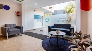 A modern reception area with two sofas, a small table with a plant, and a glass door leading to another room. - Treebo FlxHo Trio, Medanta Medicity Gurgaon (Gurugram)