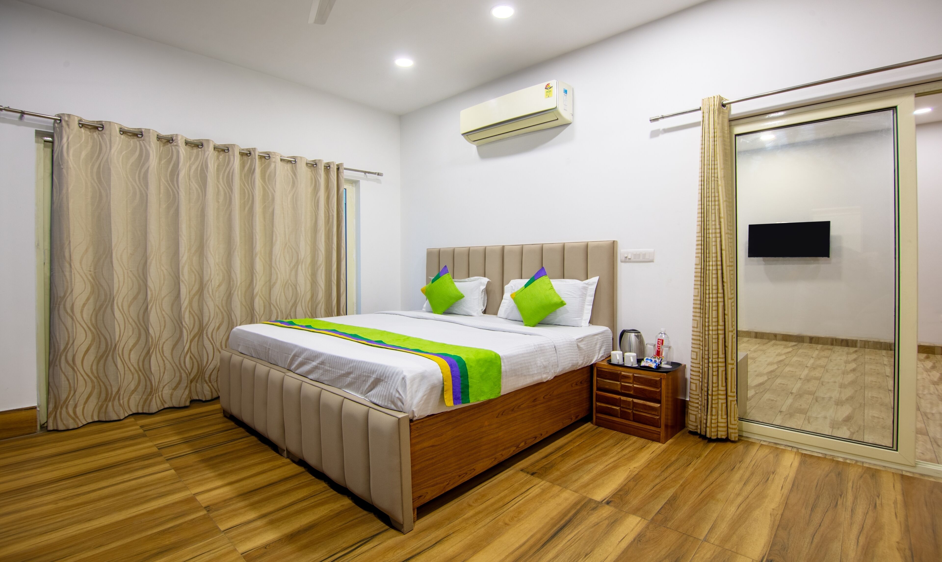 A modern hotel room with a large bed, a wooden floor, a flat-screen TV, and a sliding glass door.