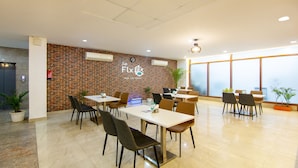 A modern dining area with brick walls, multiple tables and chairs, and large windows. - Treebo FlxHo Trio, Medanta Medicity Gurgaon (Gurugram)