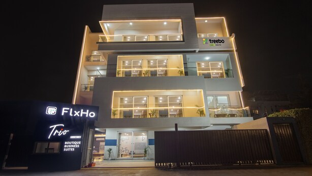 A multi-story building with illuminated windows and balconies, a sign for 'treebo' on the top floor, and a 'FlxHo' sign on the ground floor. - Treebo FlxHo Trio, Medanta Medicity Gurgaon (Gurugram)
