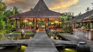 A traditional pavilion with a tiled roof, a wooden deck, and a pond.