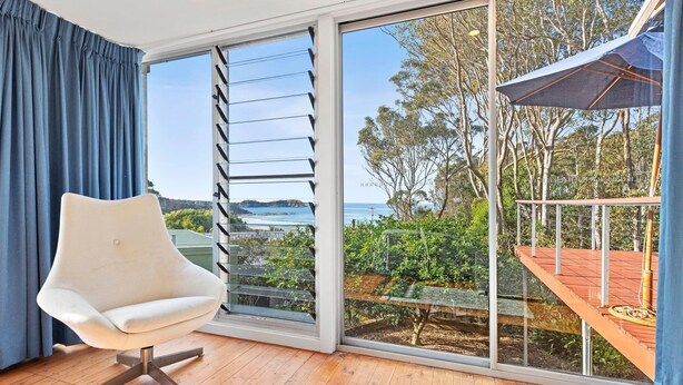 Ein modernes Zimmer mit einer großen Schiebeglasdoor zum Balkon mit Blick auf das Meer und Bäume.