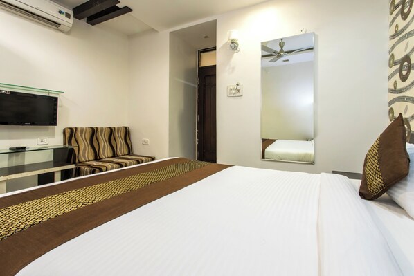 A hotel room with a bed, a TV mounted on the wall, a sofa, and a mirror.