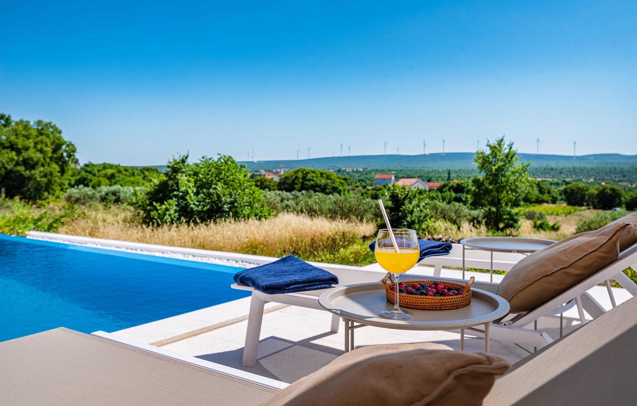 A poolside lounge with a glass of orange juice, a basket of berries, and a towel on a chair.