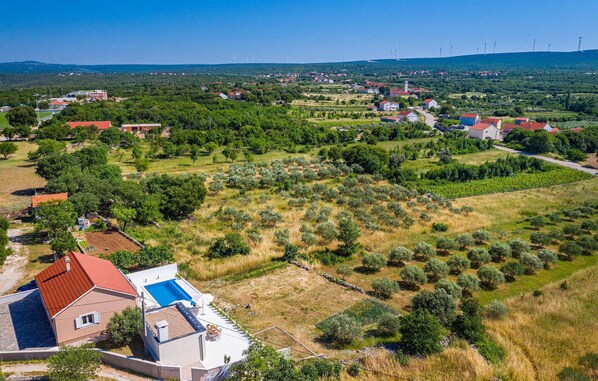 A residential area with houses, olive groves, and wind turbines in the distance.