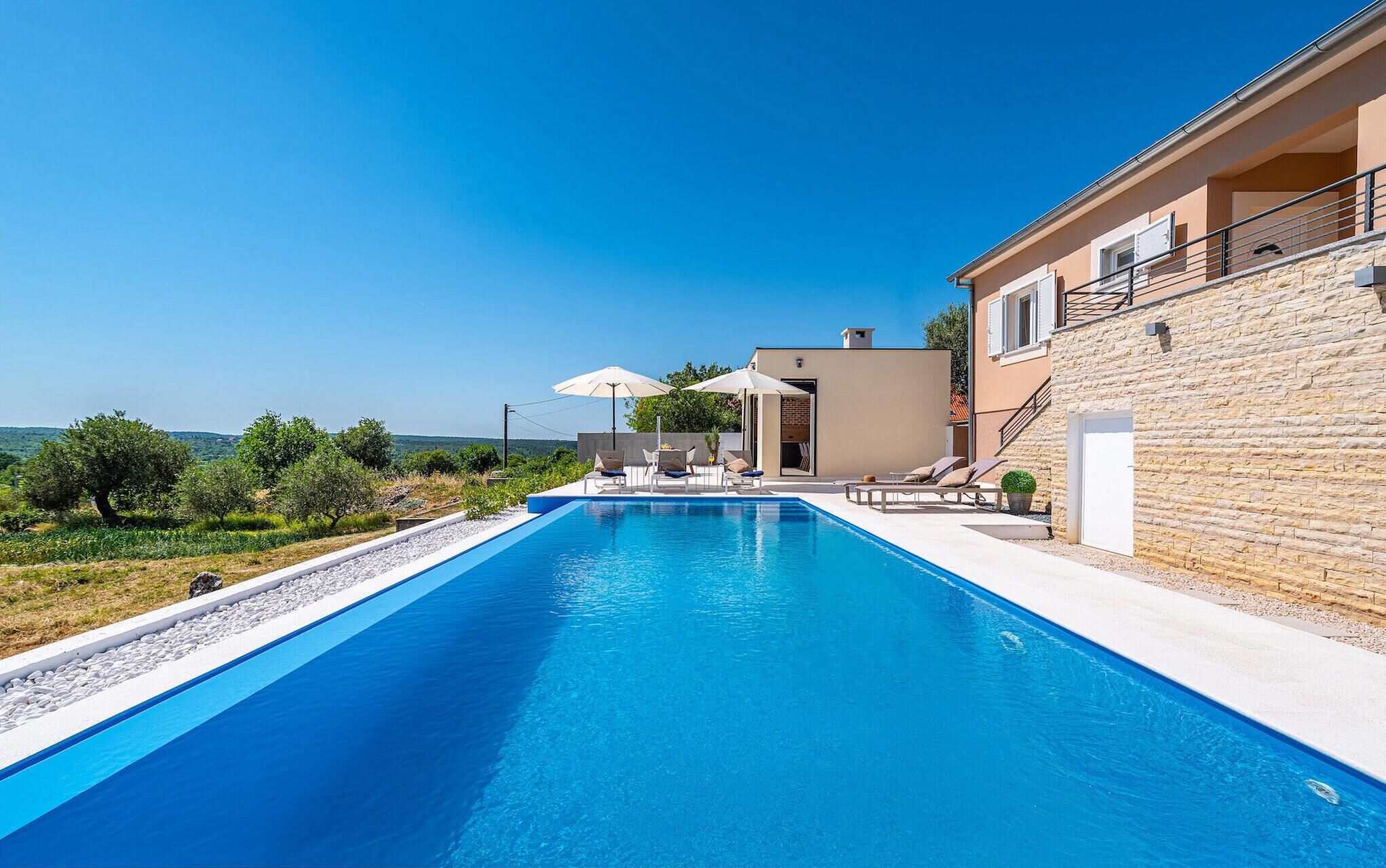 A swimming pool with lounge chairs and umbrellas, surrounded by stone walls and a view of the countryside.