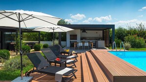 A modern outdoor pool area with lounge chairs, a dining table, and a kitchen area. - Amazing home in Rovinj (Rovinj)