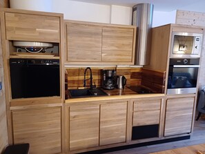Une cuisine moderne dotée de meubles en bois, d’un lave-vaisselle encastré, d’une machine à café et d’une hotte de cuisine en acier inoxydable.