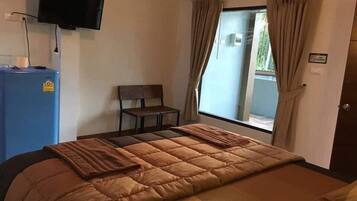 Un dormitorio con cama, una silla, televisión montada en la pared y ventana con cortinas.