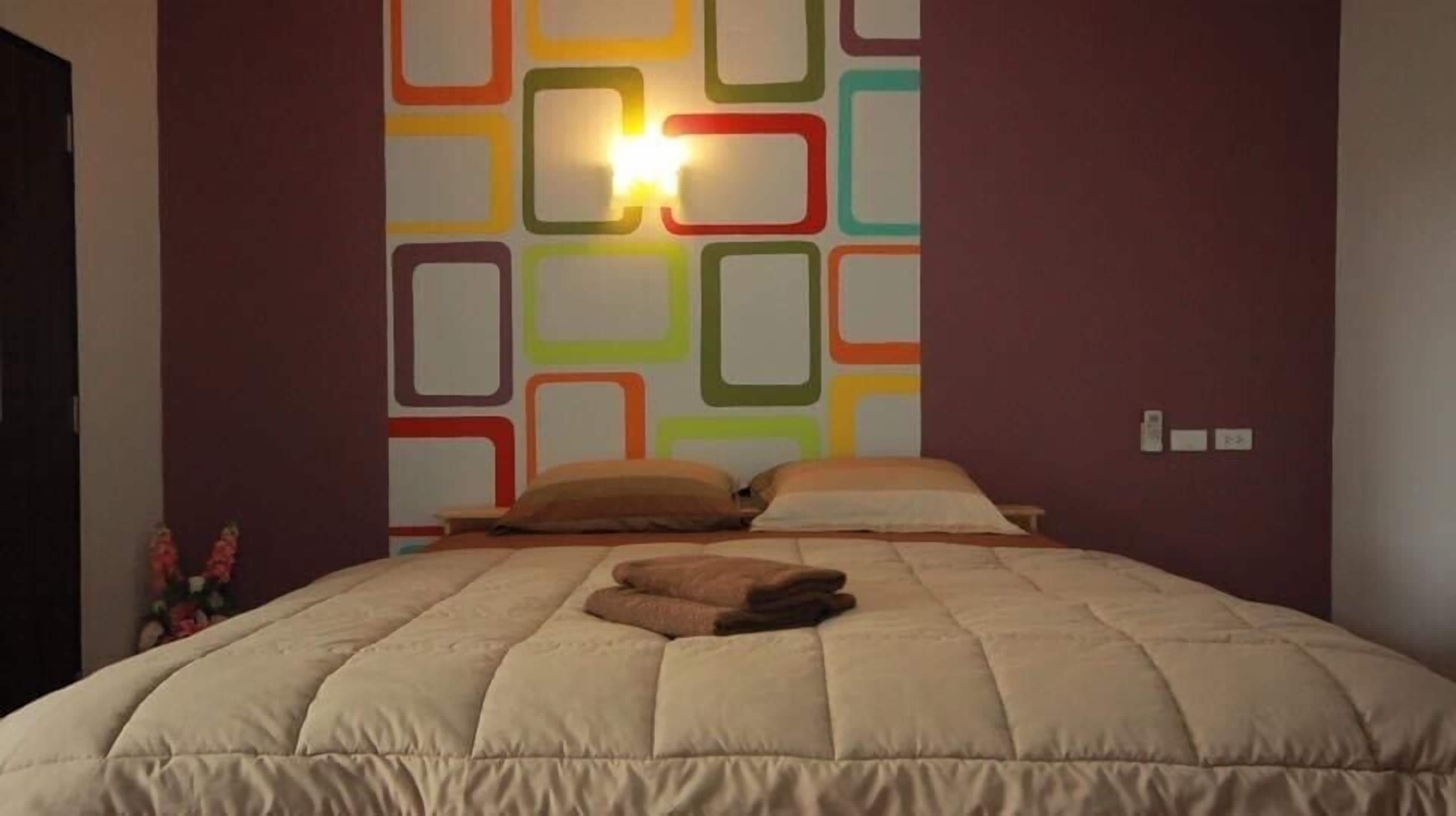 A bedroom with a bed, pillows, and a wall with colorful geometric patterns.