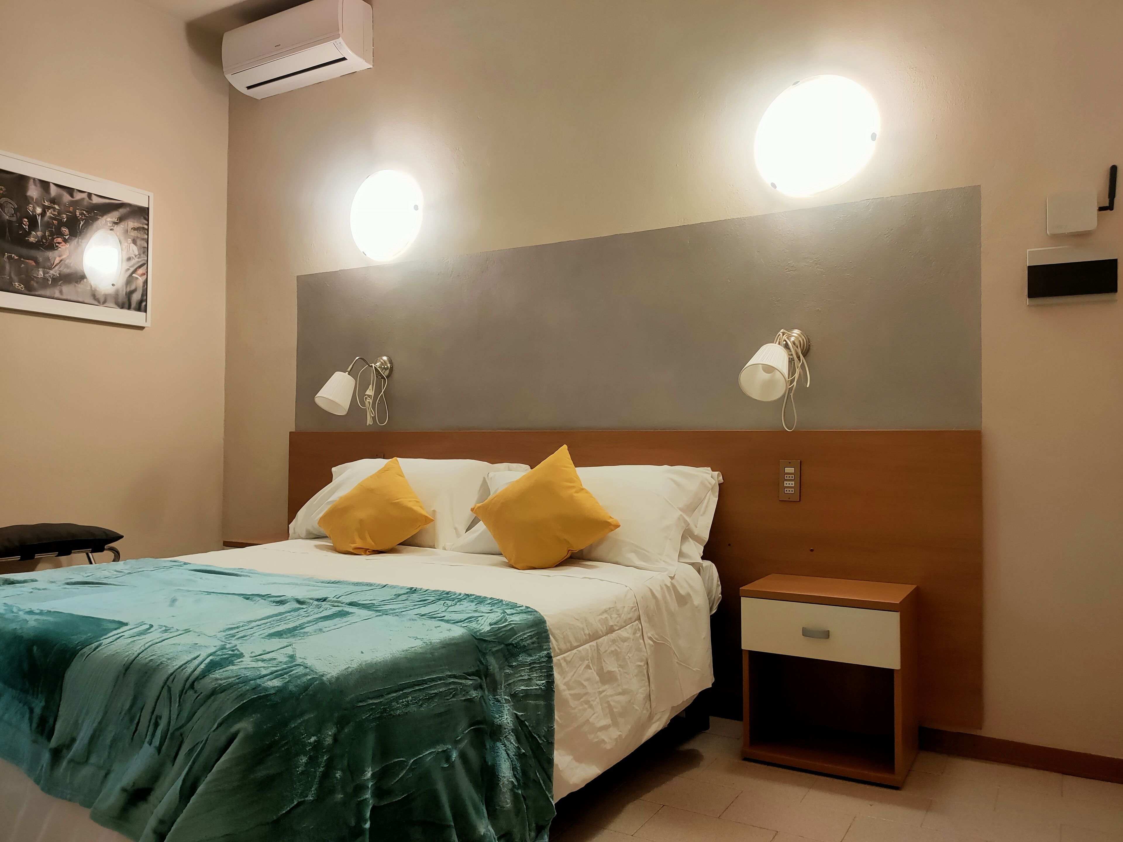 A hotel room with a bed, two bedside lamps, a nightstand, and a wall-mounted air conditioner.