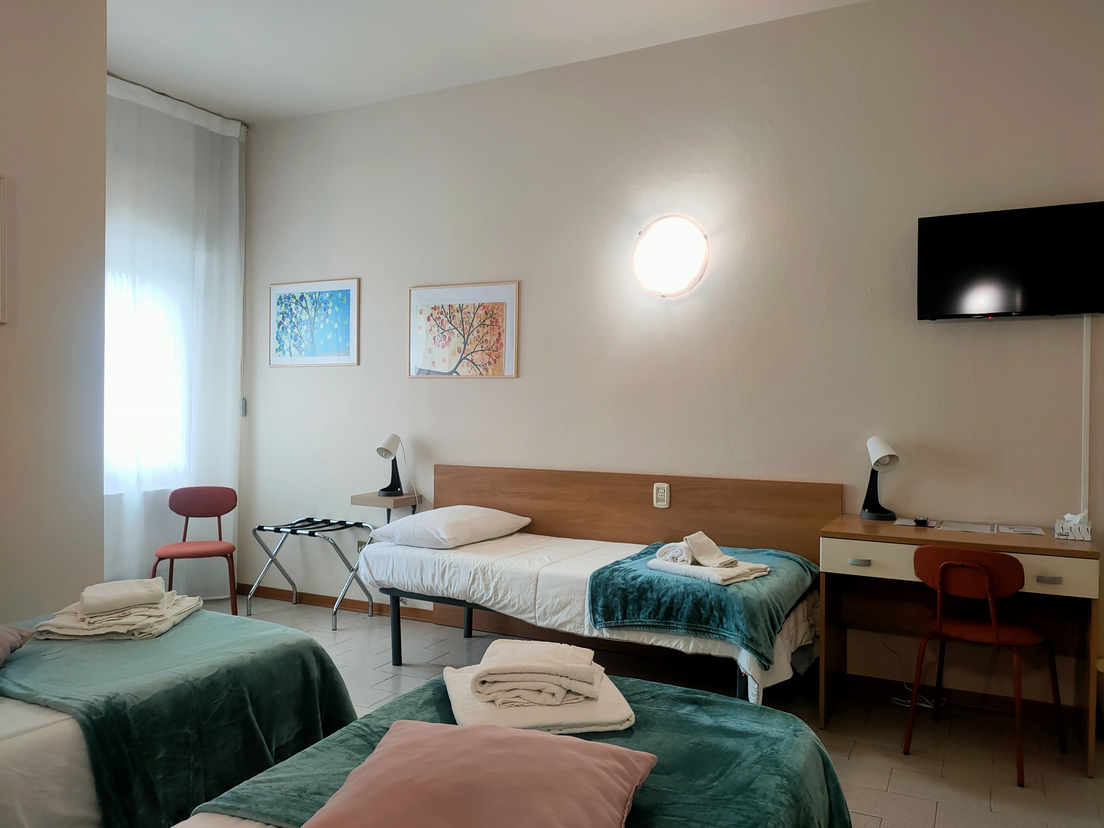 A hotel room with two beds, a desk, a chair, a TV, and artwork on the wall.