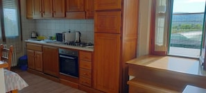 Une cuisine avec des meubles en bois, une cuisinière à gaz, un four et une fenêtre donnant sur un paysage verdoyant.