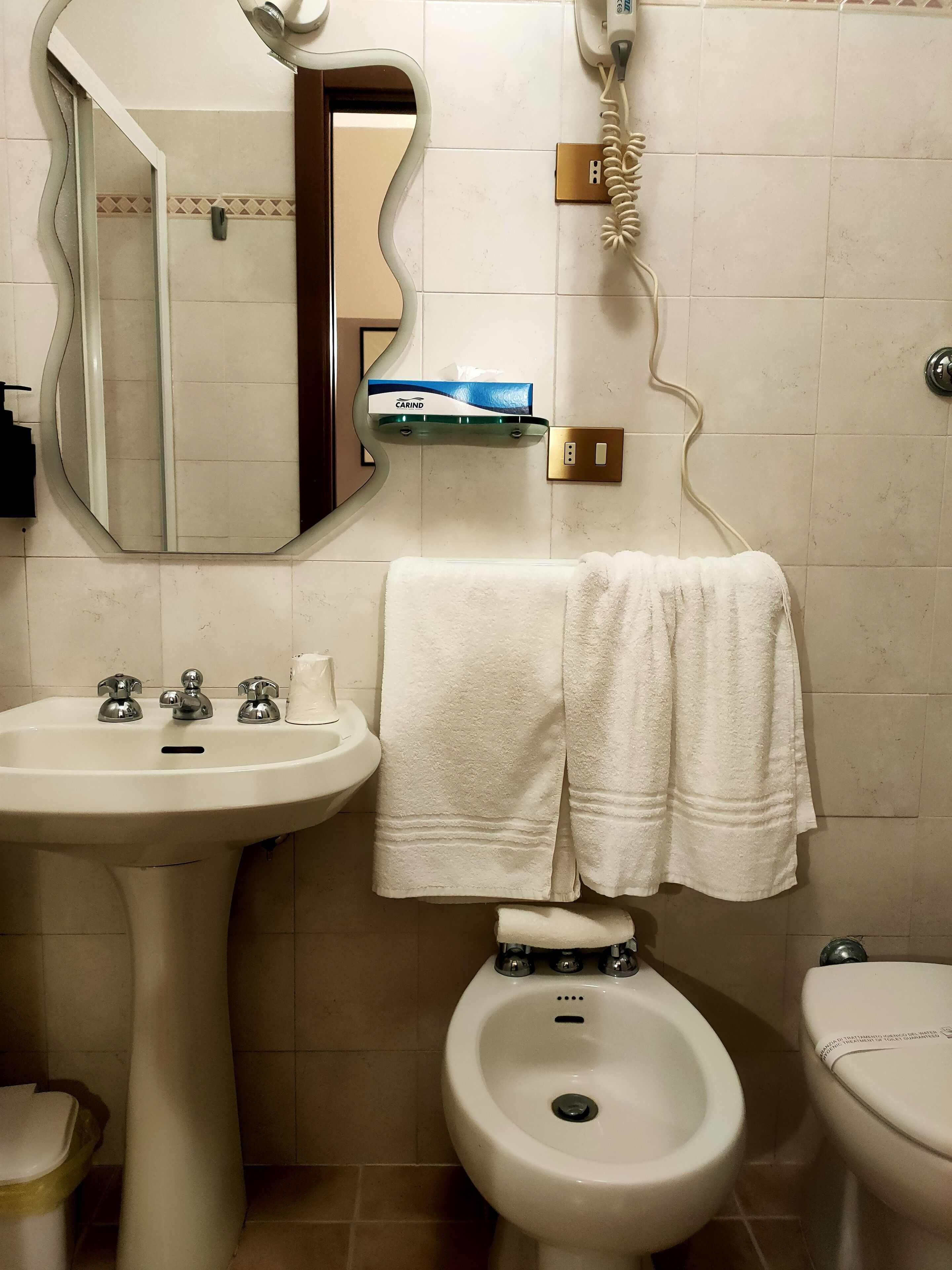 A bathroom with a pedestal sink, a bidet, a toilet, a mirror, and a towel rack.