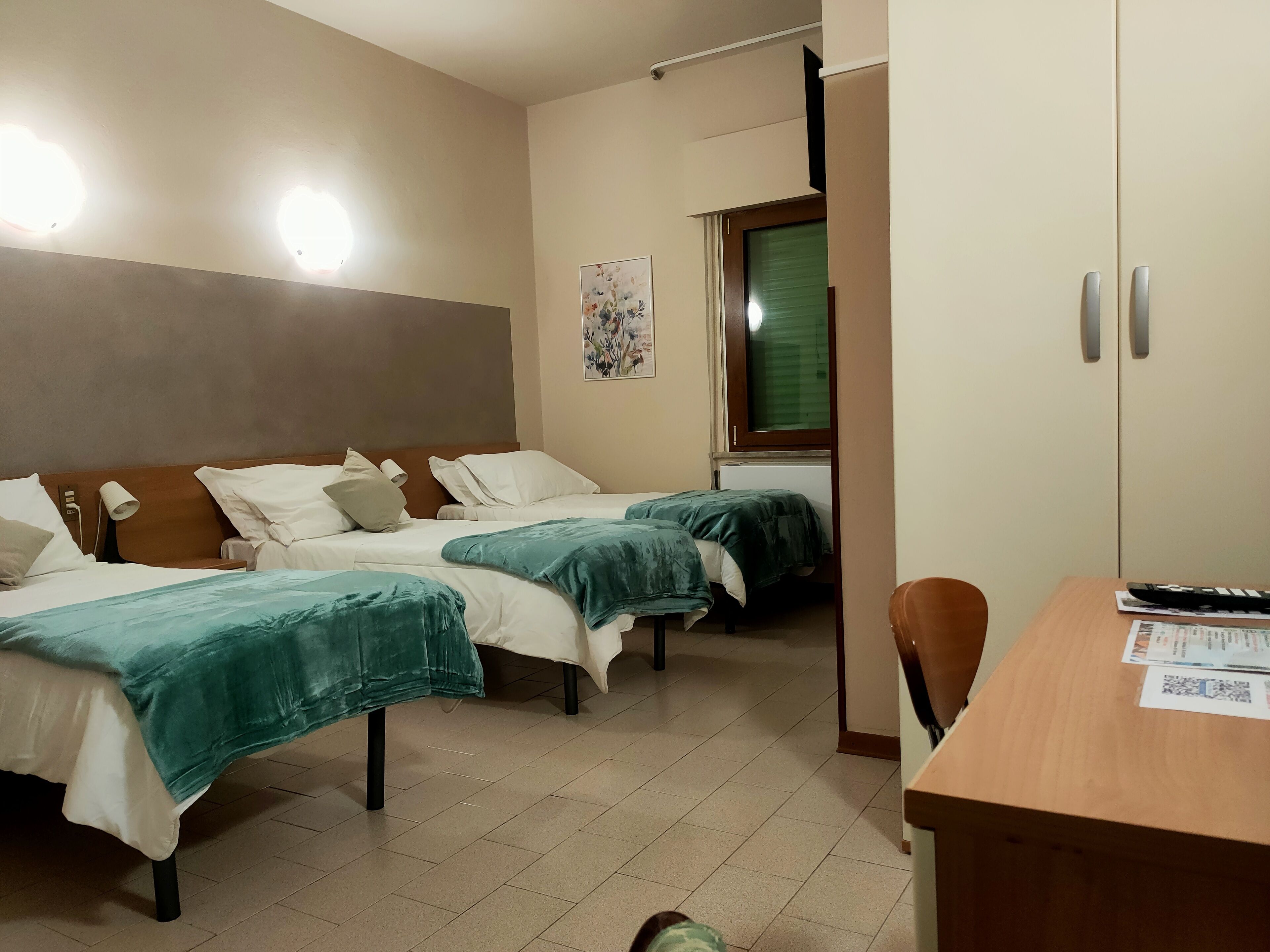 Habitación de hotel con dos camas, un escritorio, una silla y una ventana con persianas.