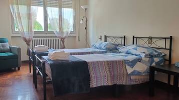 Ein Zimmer mit zwei Betten, einem Sessel, einem Tisch und einem Fenster mit Vorhängen.