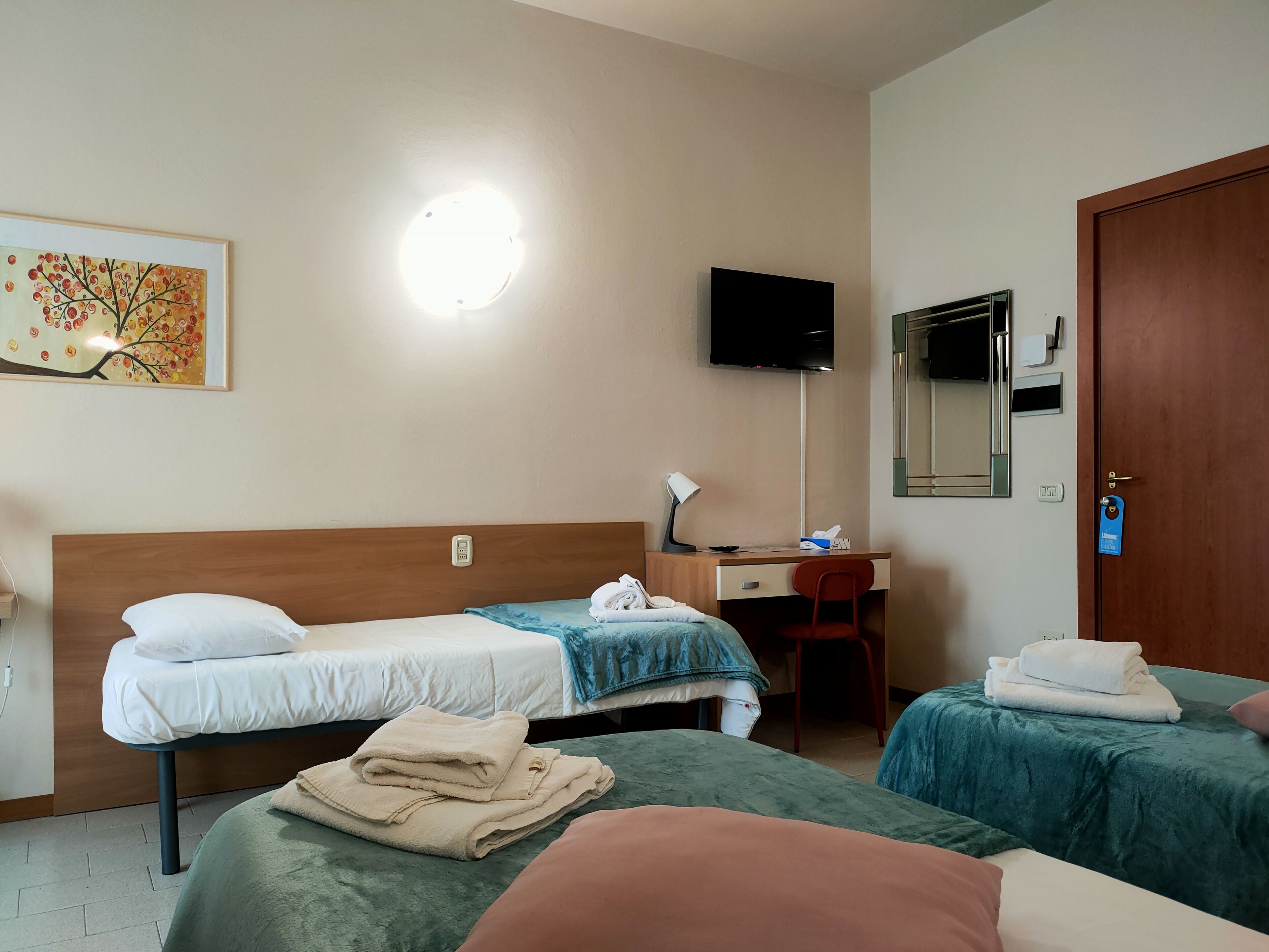 A hotel room with two beds, a desk with a computer, a TV, and a painting on the wall.