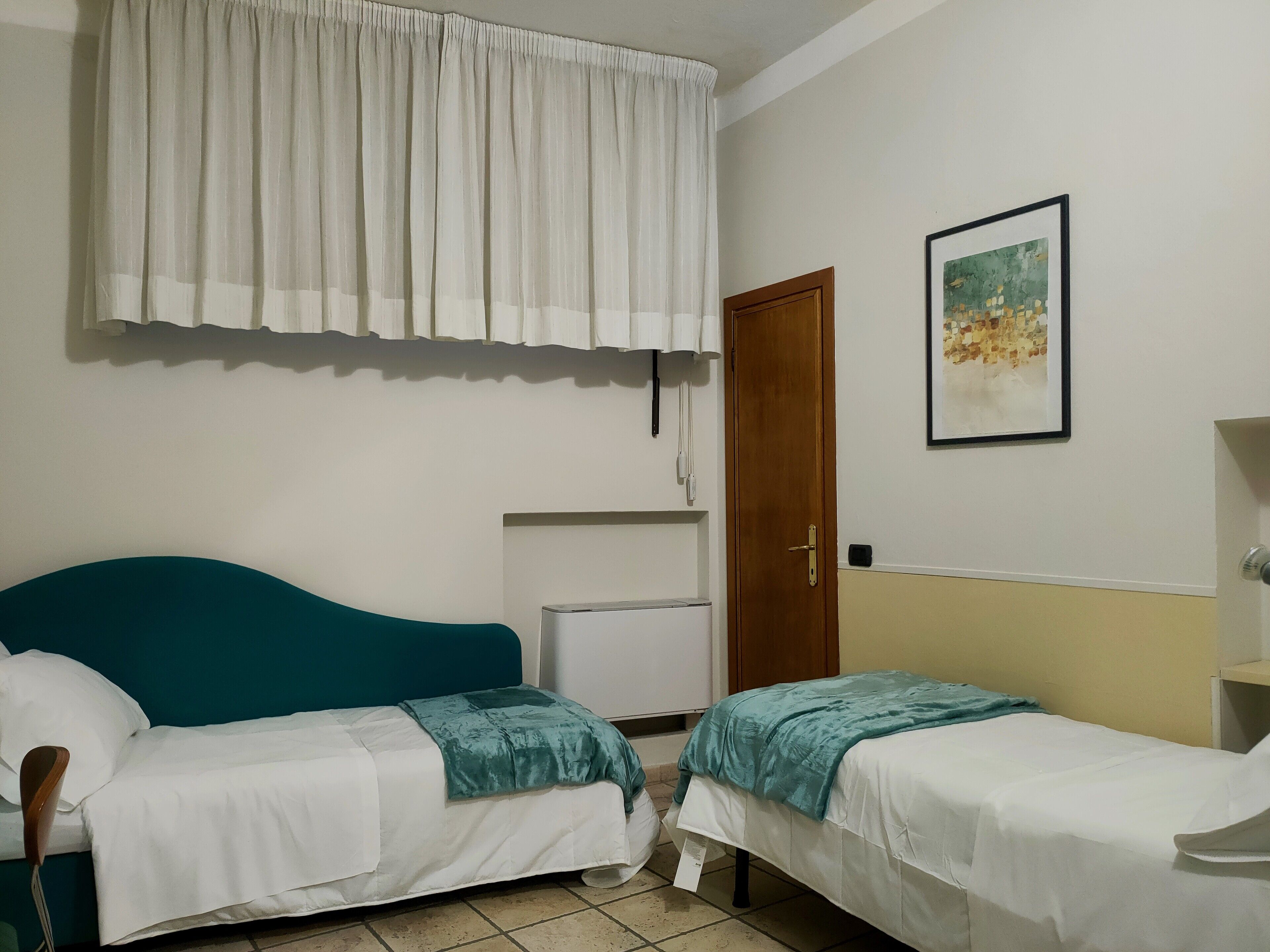 Slaapkamer met twee eenpersoonsbedden, een houten deur, een witte airconditioning en een lijst met een afbeelding aan de muur.