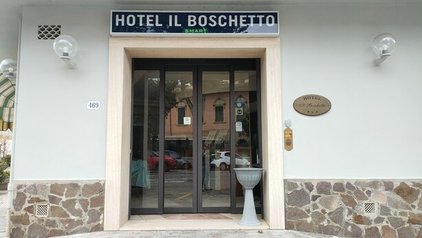 La entrada al Hotel Il Boschetto, con puerta de vidrio, fachada de piedra y un cartel.