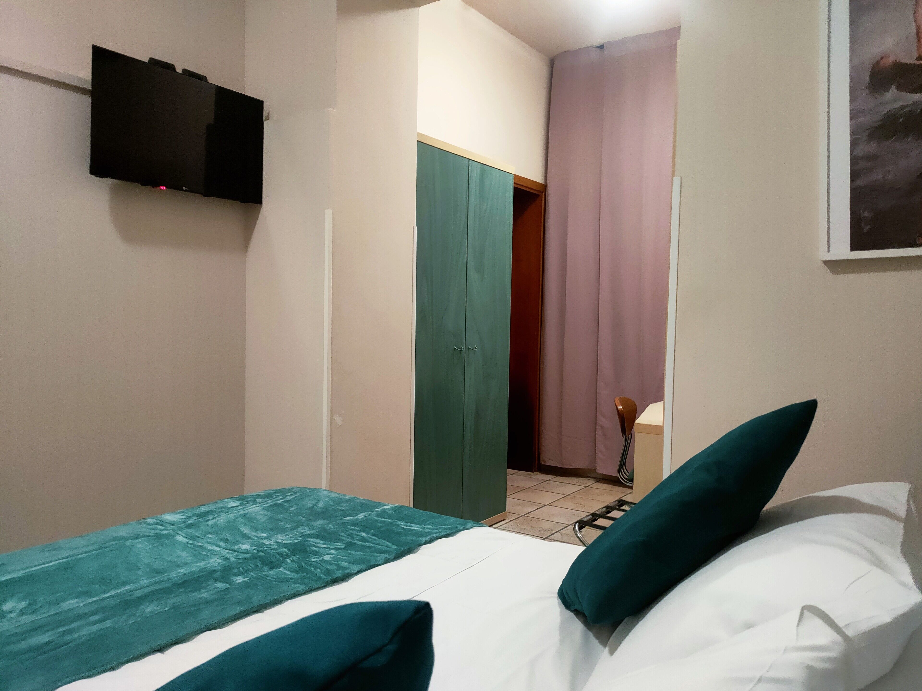 Una camera da letto con un letto, una coperta verde e bianca e un cuscino verde. C'è una televisione montata a parete.
