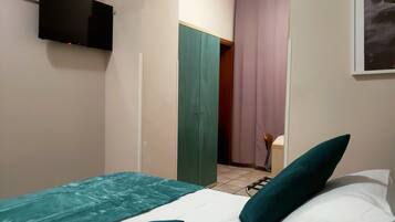 Ein Schlafzimmer mit einem Bett, einer grün-weißen Bettdecke und einem grünen Kopfkissen. An der Wand ist ein Fernseher angebracht.