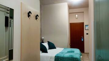 A hotel room with a bed, a desk, a mirror, and a wardrobe.
