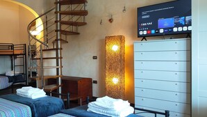 Una habitación con literas, una escalera de caracol, un escritorio, un televisor que muestra un servicio de streaming y un armario blanco grande.