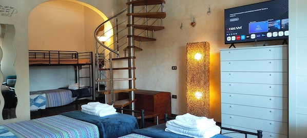Une chambre avec des lits superposés, un escalier en colimaçon, un bureau, un téléviseur diffusant un service de streaming et une grande armoire blanche.