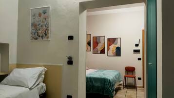Una camera d'albergo con un letto, una sedia e un tavolino. Tre quadri decorano la parete.