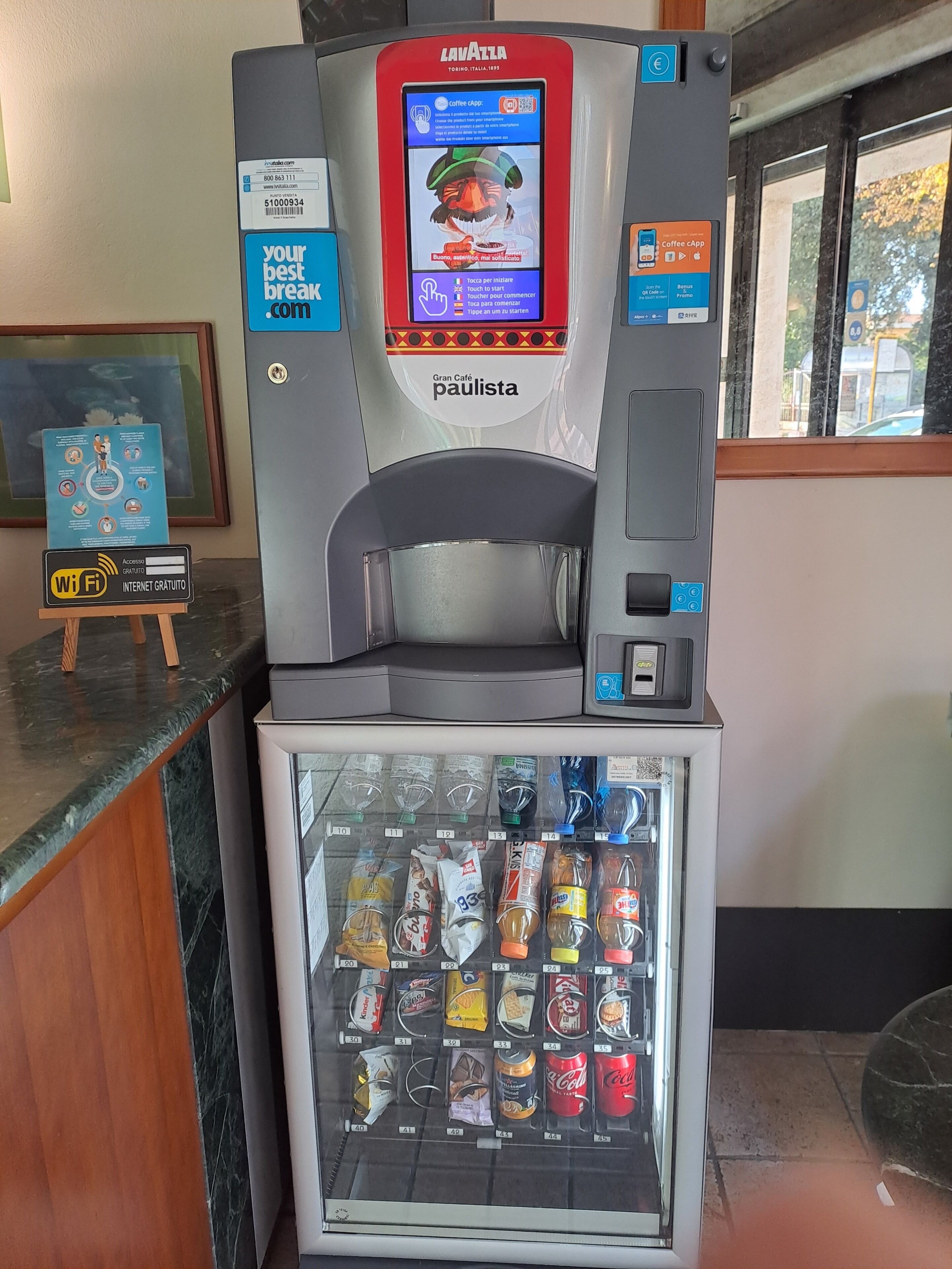Una macchina per caffè con schermo digitale e distributore automatico di bevande refrigerate sottostante.